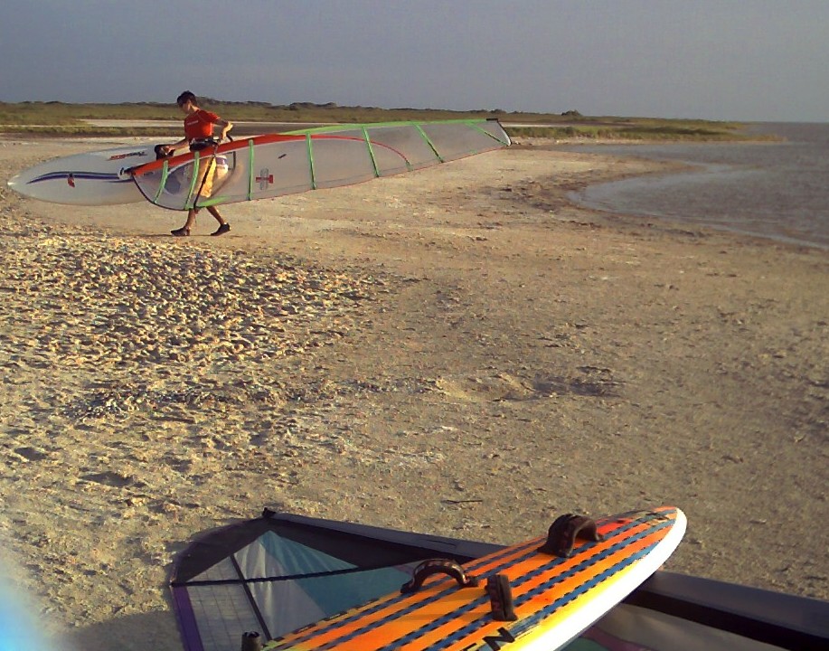Texas windsufing at Corpus Christi's Bird Island Basin, a French windsurfer brings his board onto the beach after an evening session.  Below is the colorful tail of Mike Kimbro's vintage 1989 O'Brien Epoxy Lite 9.9 windsurfer.